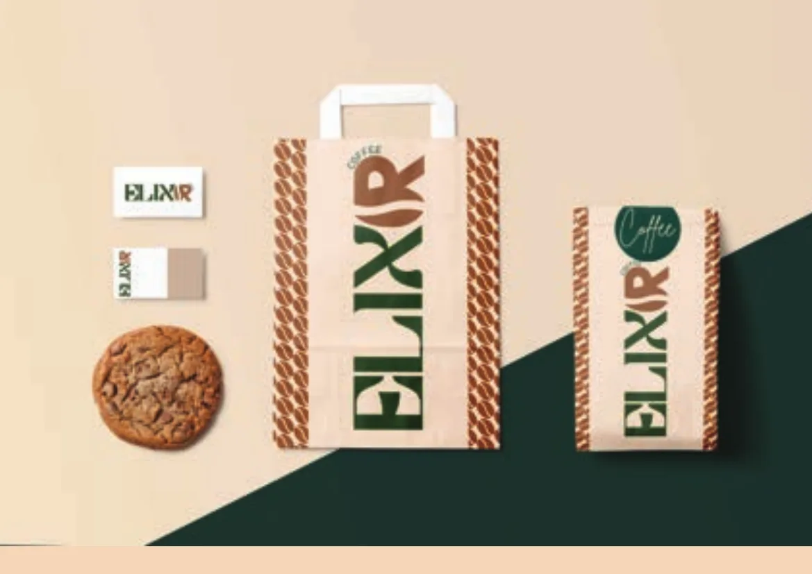 Elixir paper bag, stationery and a cookie, flat-laid on split cream and forest green